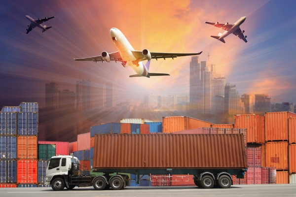 Commercial aircraft flying over shipping container yard and truck during sunset, showcasing multimodal transportation and global logistics operations