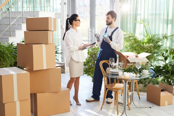 A moving professional discussing details with a woman during an international relocation, surrounded by boxes and household items.