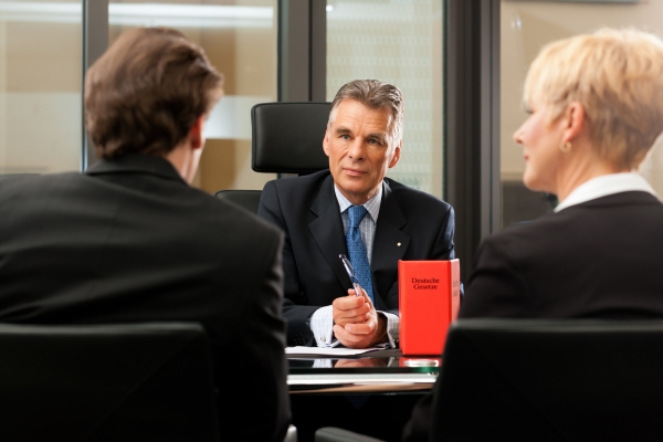 Lawyer or notary advising clients in an office setting with a legal book on the desk.