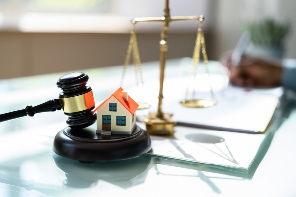 Model house on a gavel with a scale in the background, symbolizing real estate and legal regulations in Costa Rica.