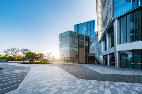 Glass office building with geometric design, empty plaza, morning sunlight