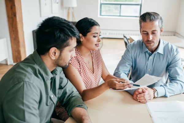 Professional tax advisors reviewing financial documents with client at office meeting table, featuring business professionals in casual business attire discussing tax implications