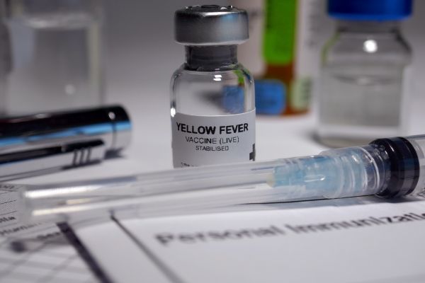 Medical vial labeled Yellow Fever vaccine with syringe on medical documentation, close-up shot in clinical setting